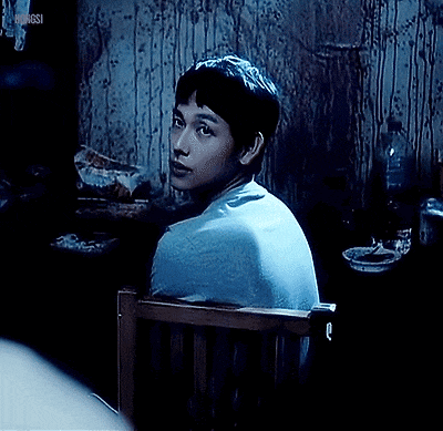 a man in a blue shirt is smiling while sitting in a chair in a dark room .