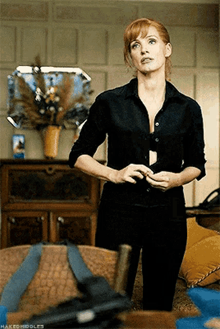 a woman in a black shirt is standing in a living room with nakedhiddles written on the bottom right
