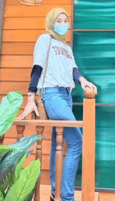 a woman wearing a hijab and a mask is standing on a railing .