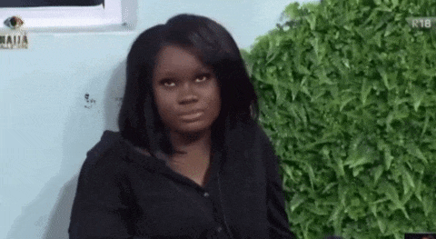 a woman in a black shirt is sitting in front of a green wall and making a funny face .