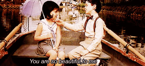 a boy and a girl are sitting in a boat and the boy is putting his hand on the girl 's neck .