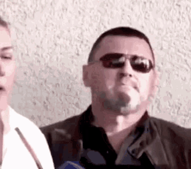 a man wearing sunglasses and a leather jacket is smoking a cigarette .