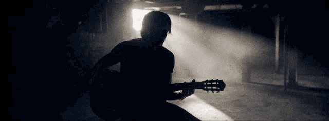 a silhouette of a person playing a guitar in a dark room