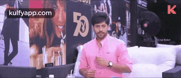 a man in a pink shirt is standing in front of a wall that says 50 .