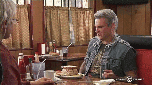 a man is sitting at a table with a plate of food and a comedy central logo