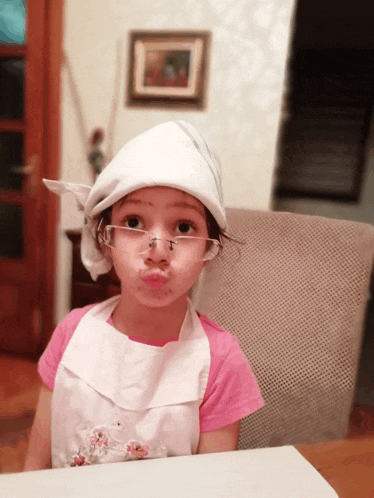 a little girl wearing glasses and an apron makes a face
