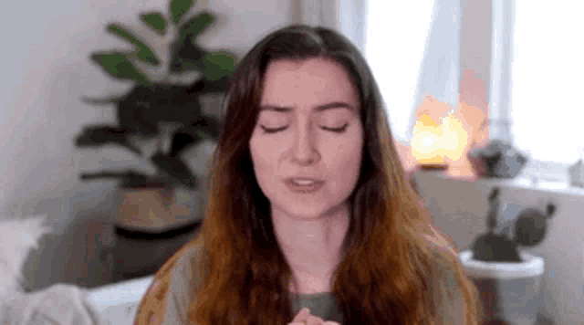 a woman with long red hair is sitting in a living room with her eyes closed and a plant in the background .