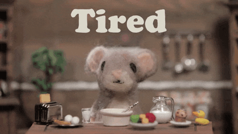 a stuffed mouse sits at a table with a bowl of cereal and the word tired above it