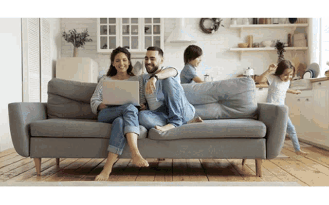 a man and woman are sitting on a couch using a laptop