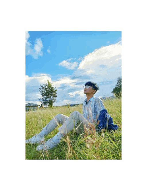 a man is sitting in the grass looking up at the blue sky