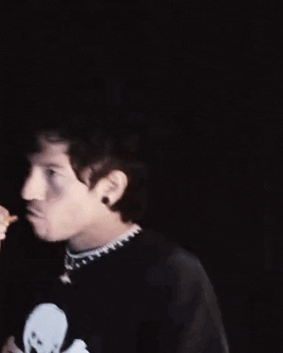 a man wearing a black shirt with a skull and crossbones on it is eating a snack