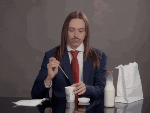 a man in a suit and tie is eating a yogurt
