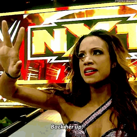 a woman in a wrestling outfit is giving a peace sign and saying back her up .