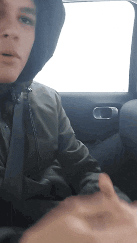 a man in a hooded jacket is sitting in the back of a car