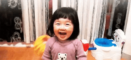 a little girl is laughing in front of a potty and a mop .