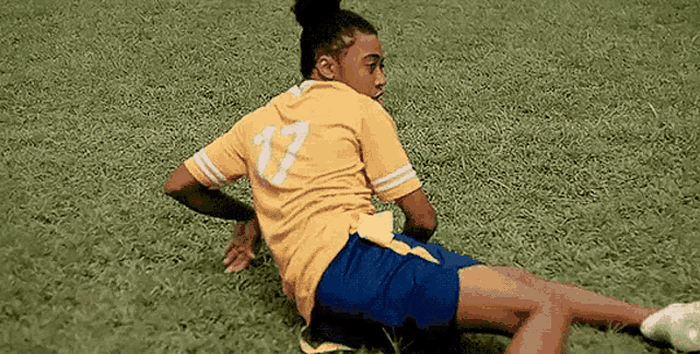 a woman in a yellow shirt and blue shorts is laying on a soccer field .