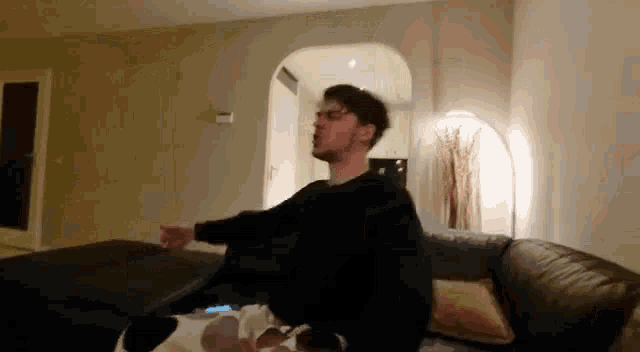 a man is sitting on a couch in a living room with his hands outstretched .
