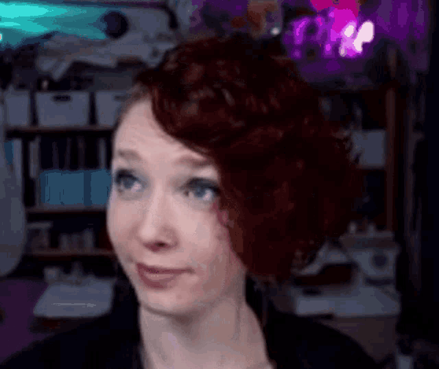 a woman with red hair and blue eyes is making a funny face in a room .