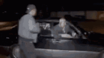 a man is standing next to a woman sitting in a car at night .