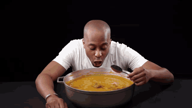 a man in a white shirt is taking a spoonful of soup from a pot
