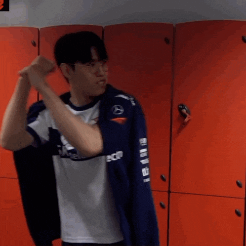 a man in a blue and white shirt is standing in a locker room with red lockers .