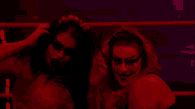 two women are standing next to each other in a dark room with red lights behind them .