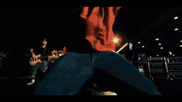 a man in a red jacket and blue jeans is playing a guitar