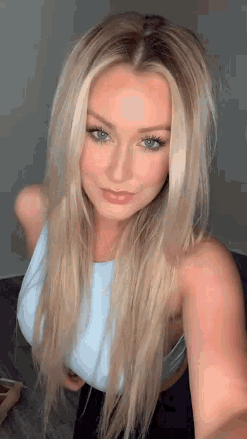 a woman with long blonde hair is taking a selfie while wearing a blue top .
