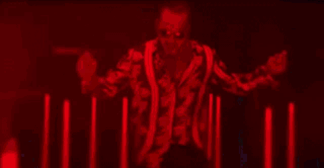 a man in a colorful shirt and sunglasses is dancing in a dark room surrounded by neon lights .