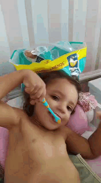 a little girl is brushing her teeth with a toothbrush in front of a bag of pampers .