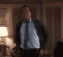 a man in a suit and tie is standing in a living room with his hands in his pockets .