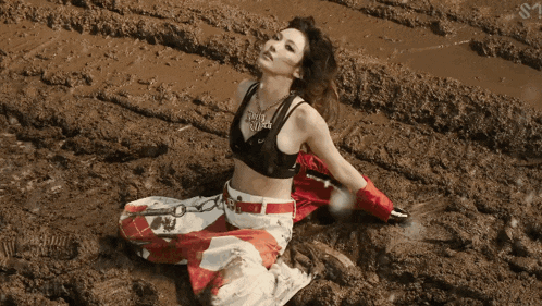 a woman in a crop top sits in the mud with the letter s on the bottom right