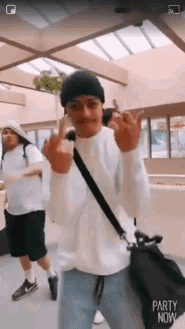 a man wearing a white sweater and a black hat is giving the middle finger .