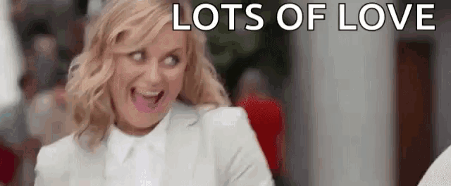 a woman in a white suit and white shirt is making a funny face while saying `` lots of love '' .