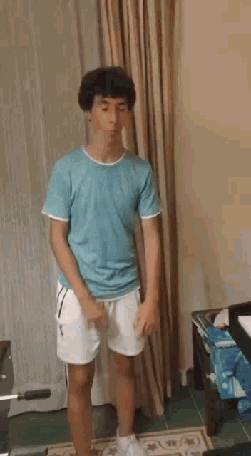 a young man in a blue shirt and white shorts is standing in front of a curtain .