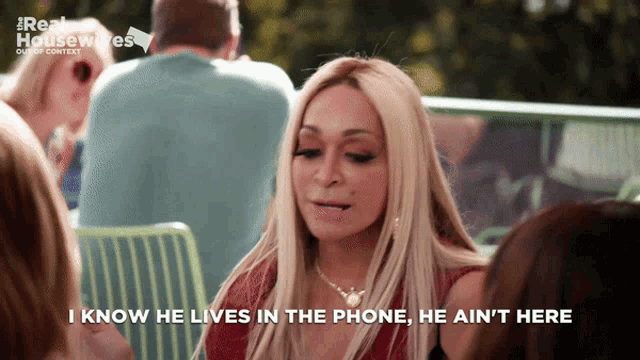 a woman sitting at a table says " i know he lives in the phone he ain 't here "