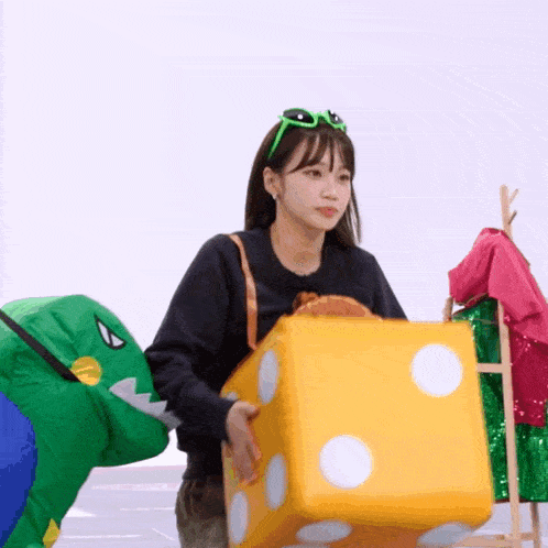 a woman in a dinosaur costume is carrying a large yellow dice