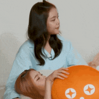 two women are laying on a couch one is holding an orange pillow with a star on it