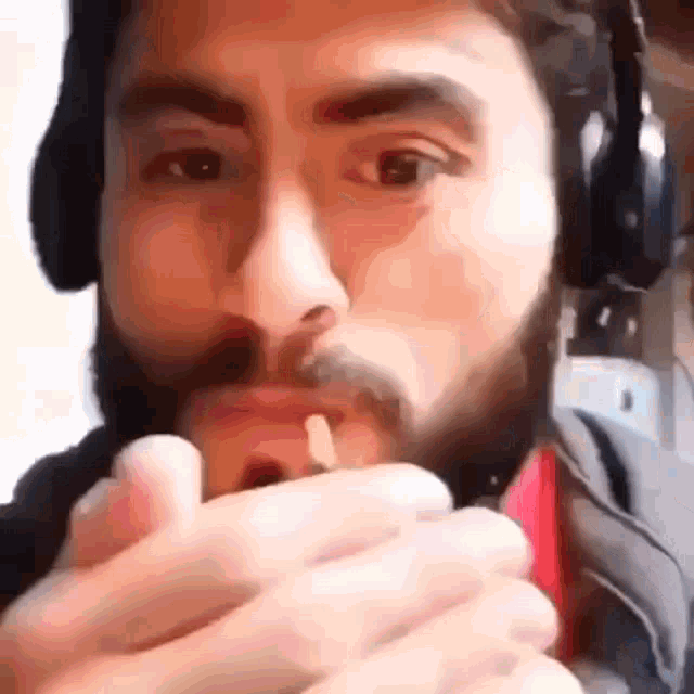 a man with a beard and headphones is holding a lighter in his mouth .