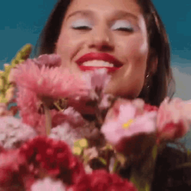 a woman is smiling while holding a bouquet of pink flowers in front of her face .