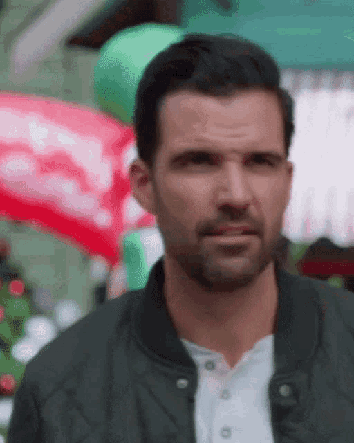 a man with a beard wearing a black jacket is standing in front of a christmas tree .
