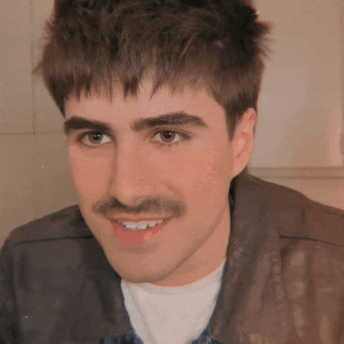a young man with a mustache is smiling and looking at the camera