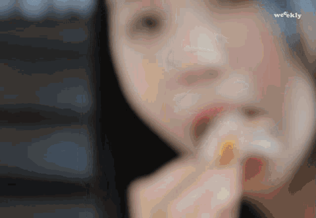 a blurry picture of a woman eating a sandwich with weekly written in the corner