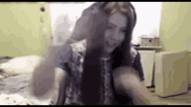 a woman with long hair is sitting on a bed wearing headphones and smiling .