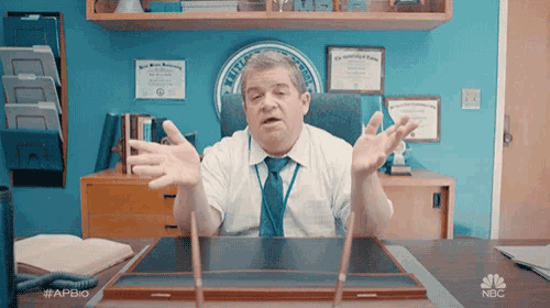 a man is sitting at a desk with a nbc logo on the desk