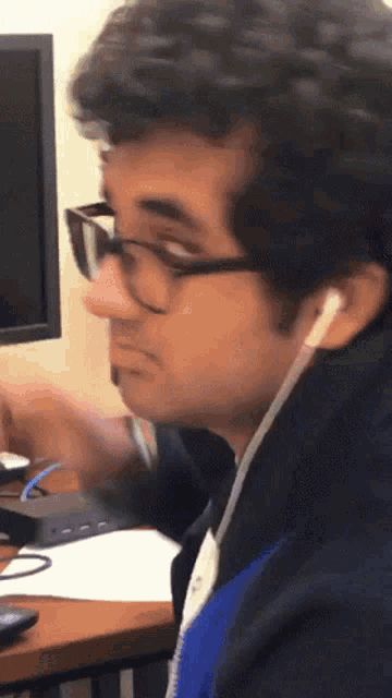 a man wearing glasses and ear buds sits at a desk
