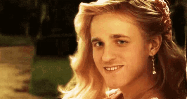 a close up of a woman with long blonde hair and earrings smiling .