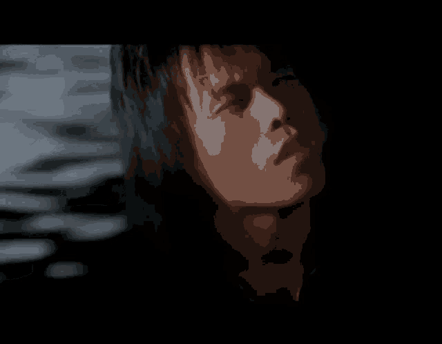 a man with long hair is smoking a cigarette in a dark room .