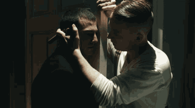 a man in a white shirt holds another man 's head in a dark room