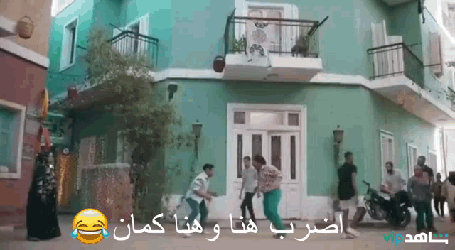 a group of people are dancing in front of a green building with arabic writing